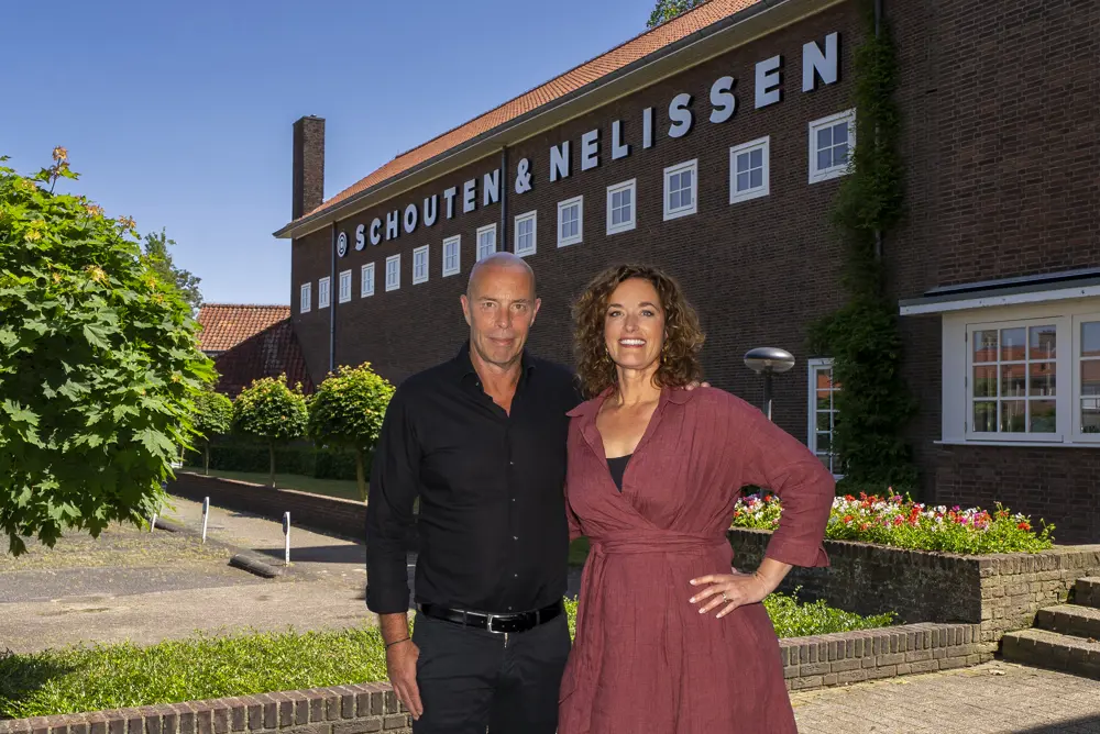 Twee vertegenwoordigers staan voor het gebouw van Schouten & Nelissen op de foto bij het bericht over de eigendomsoverdracht in mei 2026.